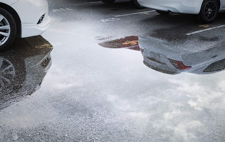 Stor vattenpöl på parkering med minst tre bilar.